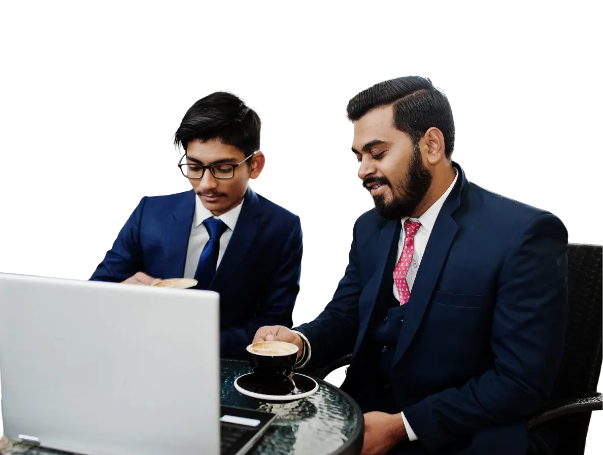 Two business professionals in suits sit at a glass table with a laptop, each holding a cup of coffee as they look at the screen.