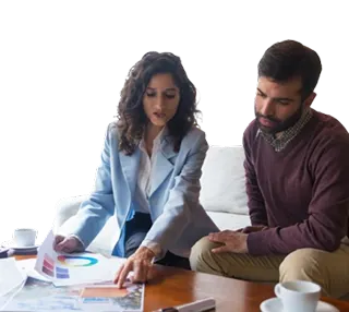Two colleagues review charts and documents on a table during a meeting with coffee nearby.