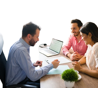 Three professionals in a meeting: a man in blue writes on a pad while two colleagues smile near a laptop on the table.